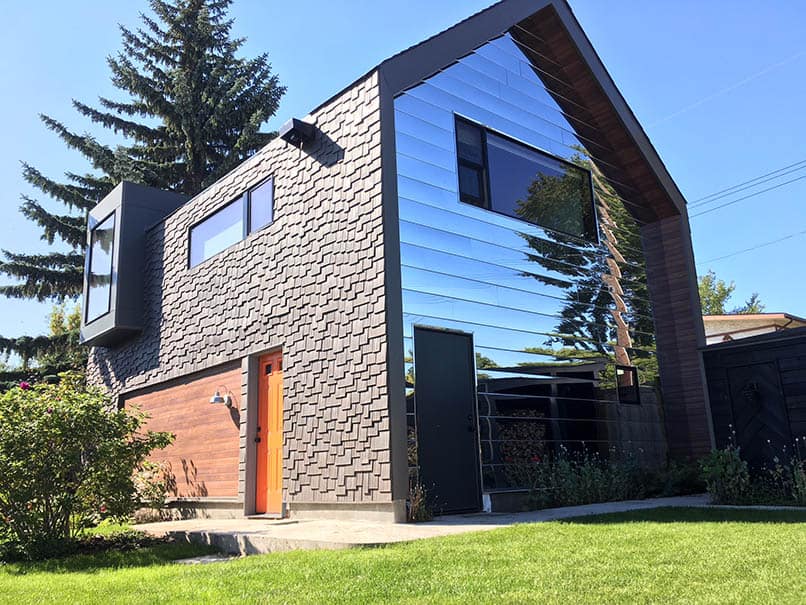 Home with reflective siding, Enviroshake cedar composite siding, and an orange door with blue skies and green grass
