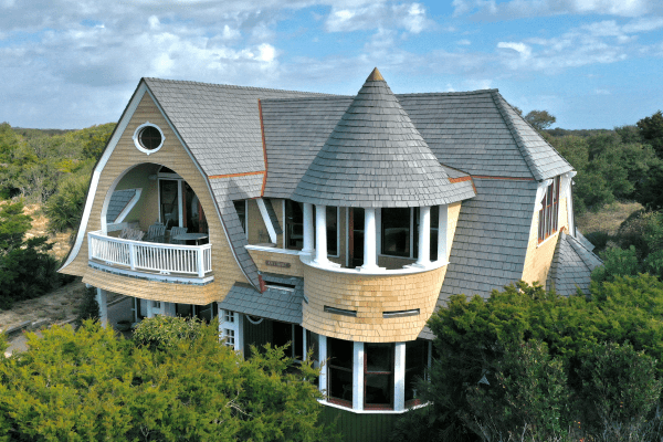 Distinctive coastal-style home with an Enviroshake synthetic cedar roof, featuring a turret with columned windows and a curved balcony overlooking lush greenery.