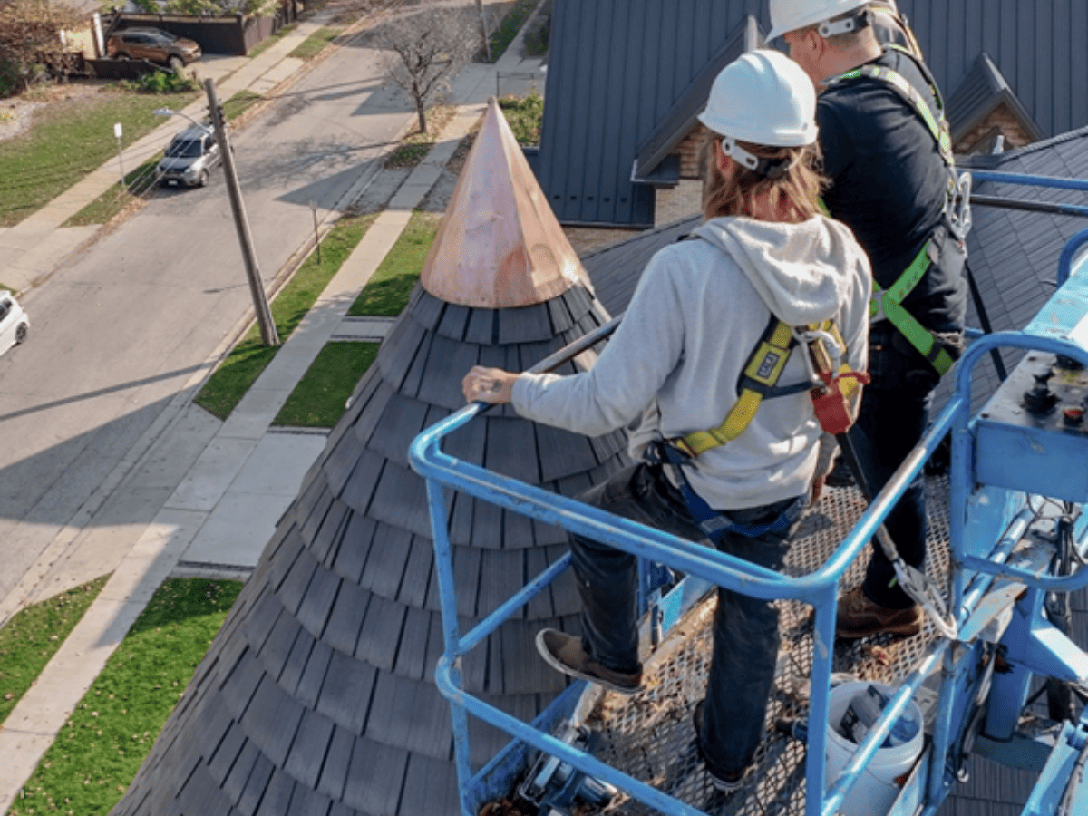 Closeup of roofing contractors on a lift installing Enviroshake to a roof turret with a copper cap