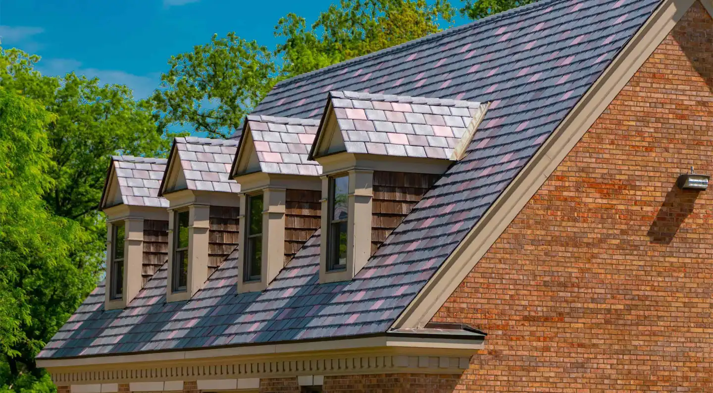 Close-up of multitone Enviroslate roof with dormer windows on a brick home under a clear blue sky.